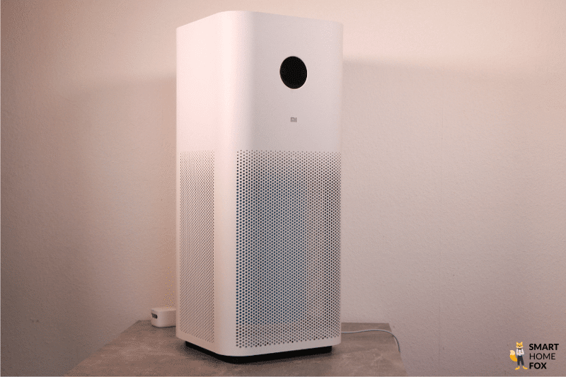 Очиститель воздуха Xiaomi Mi Air Purifier Pro H стоит на столе перед белой стеной.
